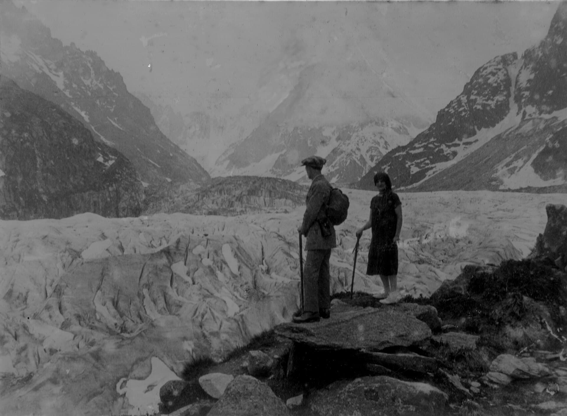 Two visitors look across the Mer de Glace towards steep mountain walls in June 1926.
