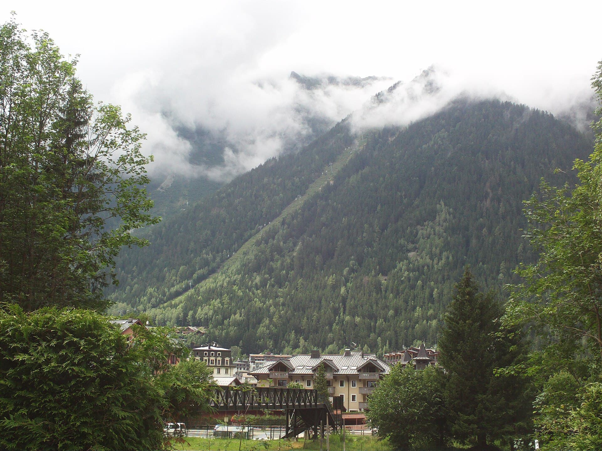 Chamonix's roofs and trees sit below cloud-covered mountain walls in a 2014 view from the Montenvers railway.