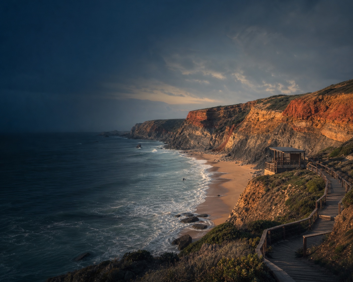 Praia do Amado surf beneath its layered rust-coloured cliffs