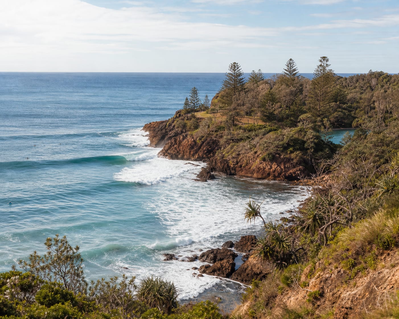 Angourie point surf curling past its rust-red rocks and coastal bush