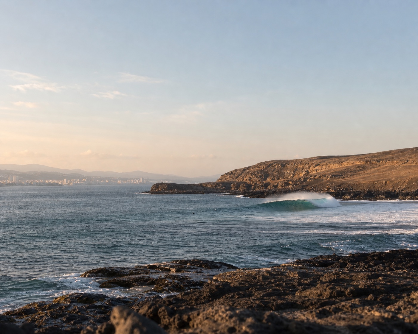 A reef wave beside the volcanic cliffs of El Confital with Las Palmas in the distance
