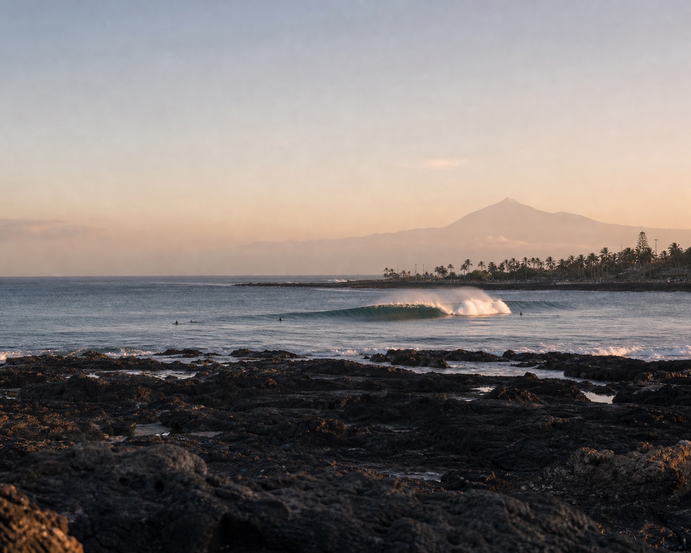 A reef wave breaking off Tenerife's volcanic coast beneath the distant silhouette of Teide